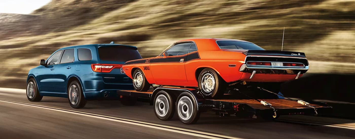A blue 2024 Dodge Durango is towing an orange car on a trailer.