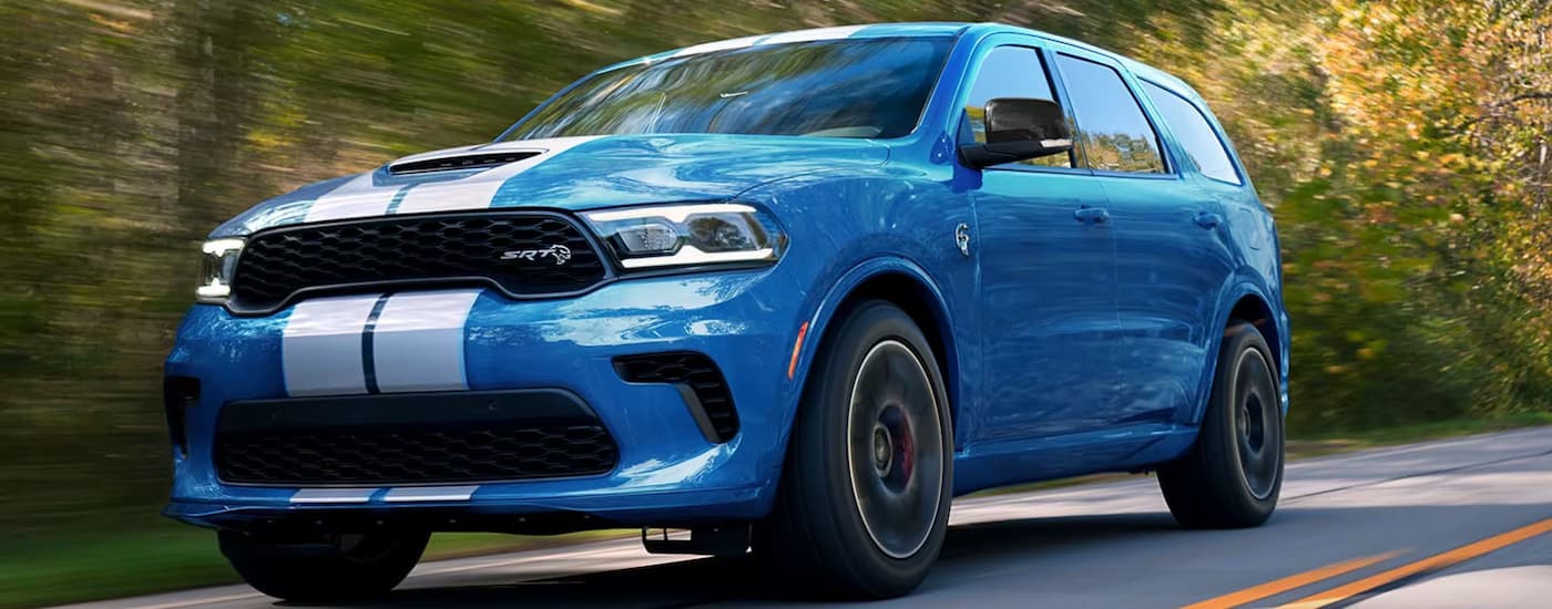 A blue 2024 Dodge Durango SRT is driving on a tree-lined road.
